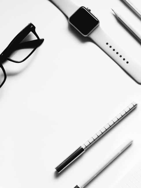A sleek black-and-white flat lay of a modern office desk featuring a smartwatch and glasses.